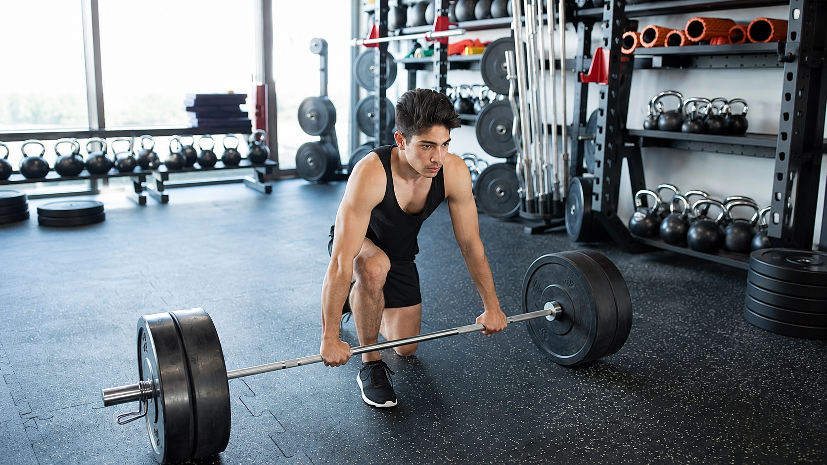 Man performing deadlift with Olympic barbell in well-equipped gym with kettlebells and weight racks