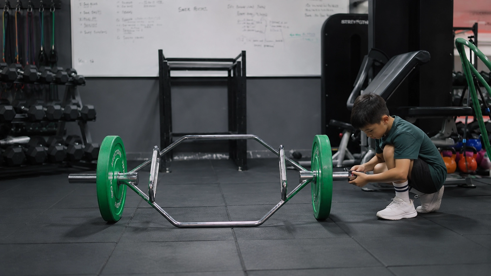 Person setting up a trap bar with green weight plates for a deadlift exercise in a gym