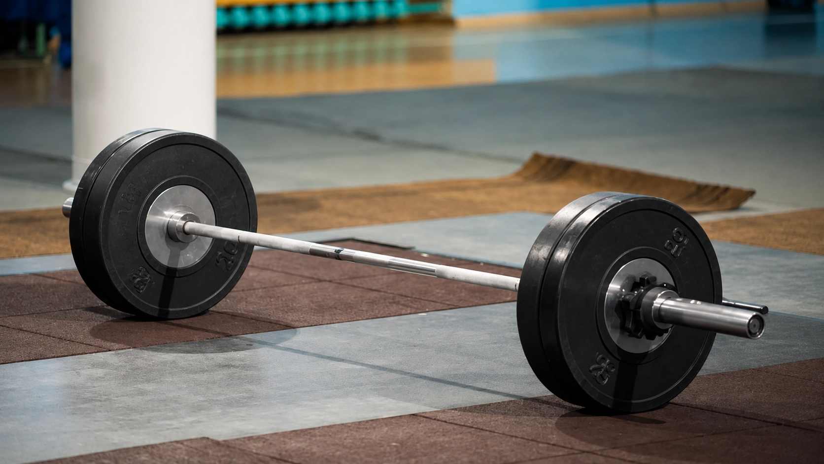 Two loaded barbells with black weight plates on a gym floor comparing Olympic and standard barbell types
