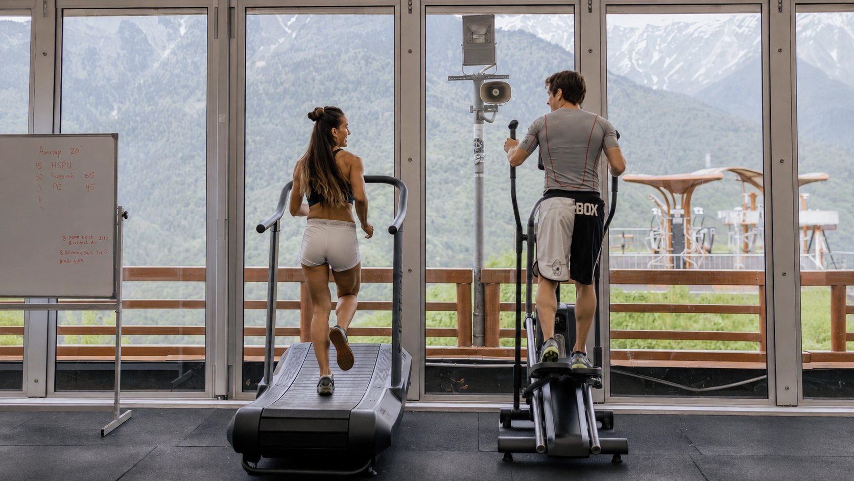 Woman running on treadmill and man using elliptical machine side by side in gym