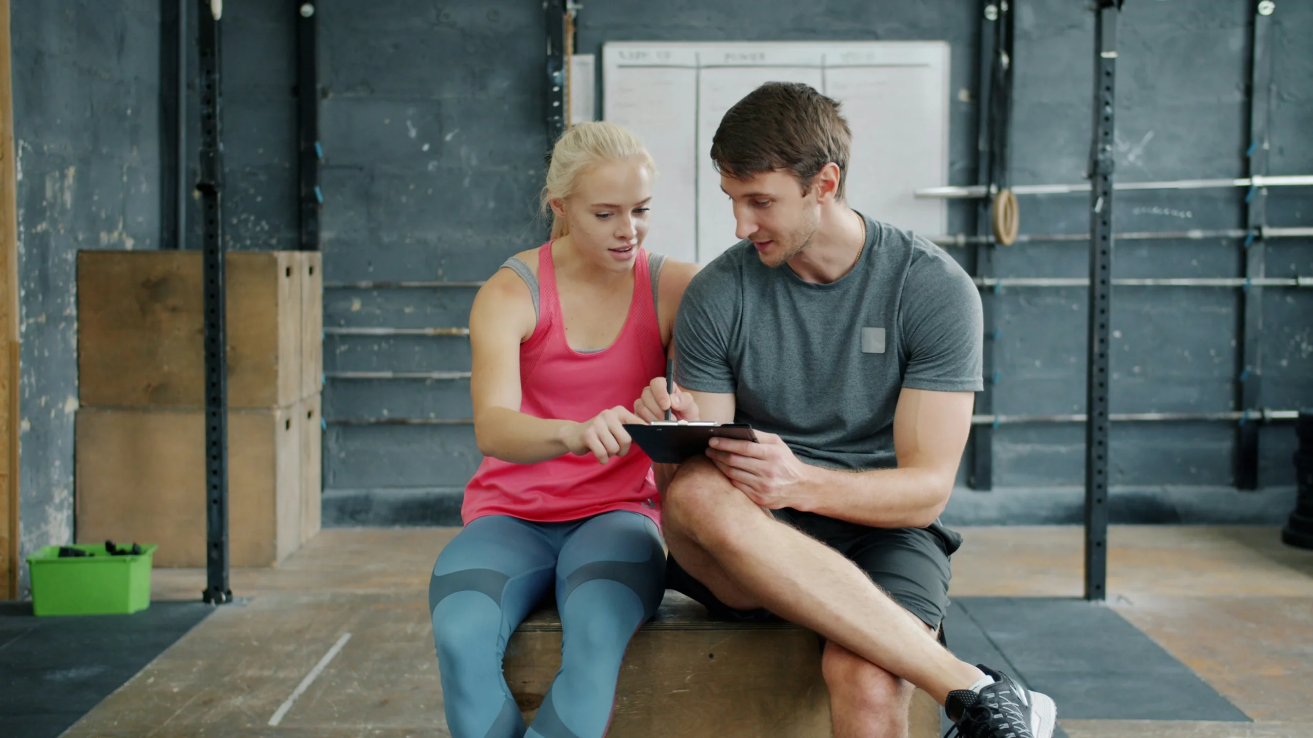 Trainer and woman reviewing fitness plan and budget goals on tablet in gym