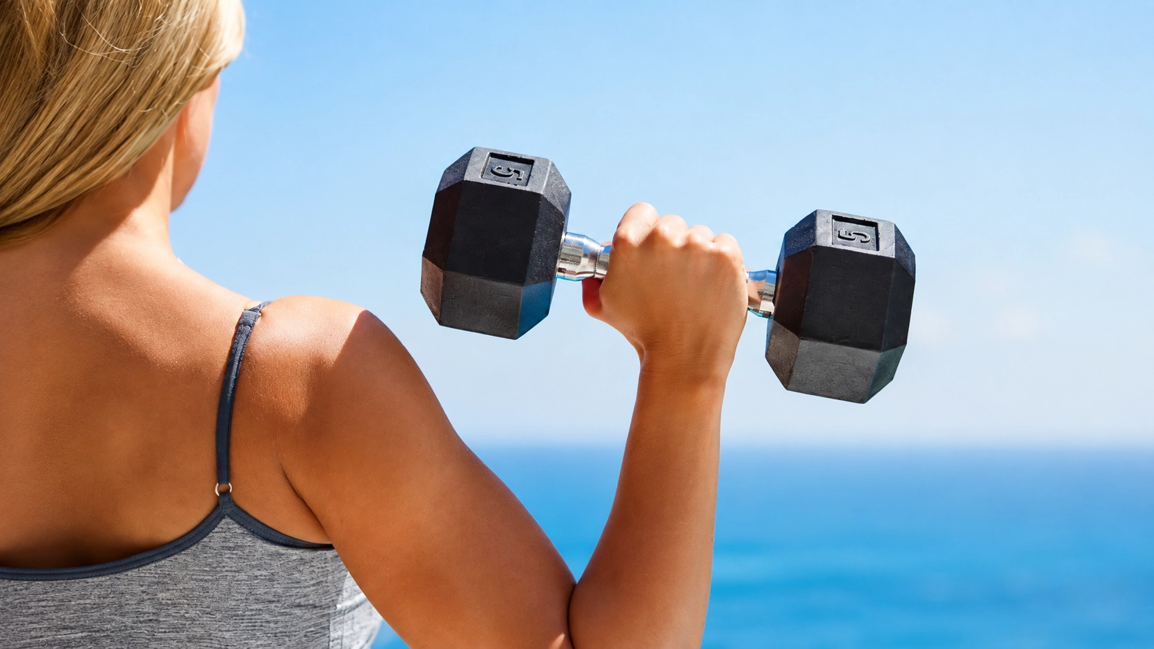 Woman holding non-slip grip hex dumbbell outdoors against ocean backdrop