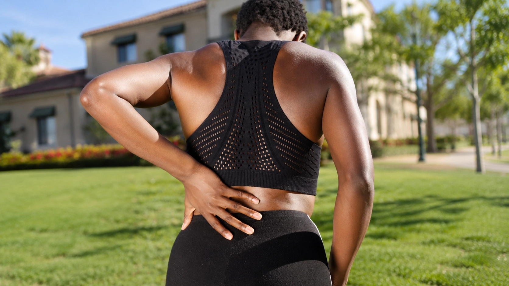 Woman experiencing lower back discomfort while outdoors, demonstrating the importance of proper spinal support during fitness activities