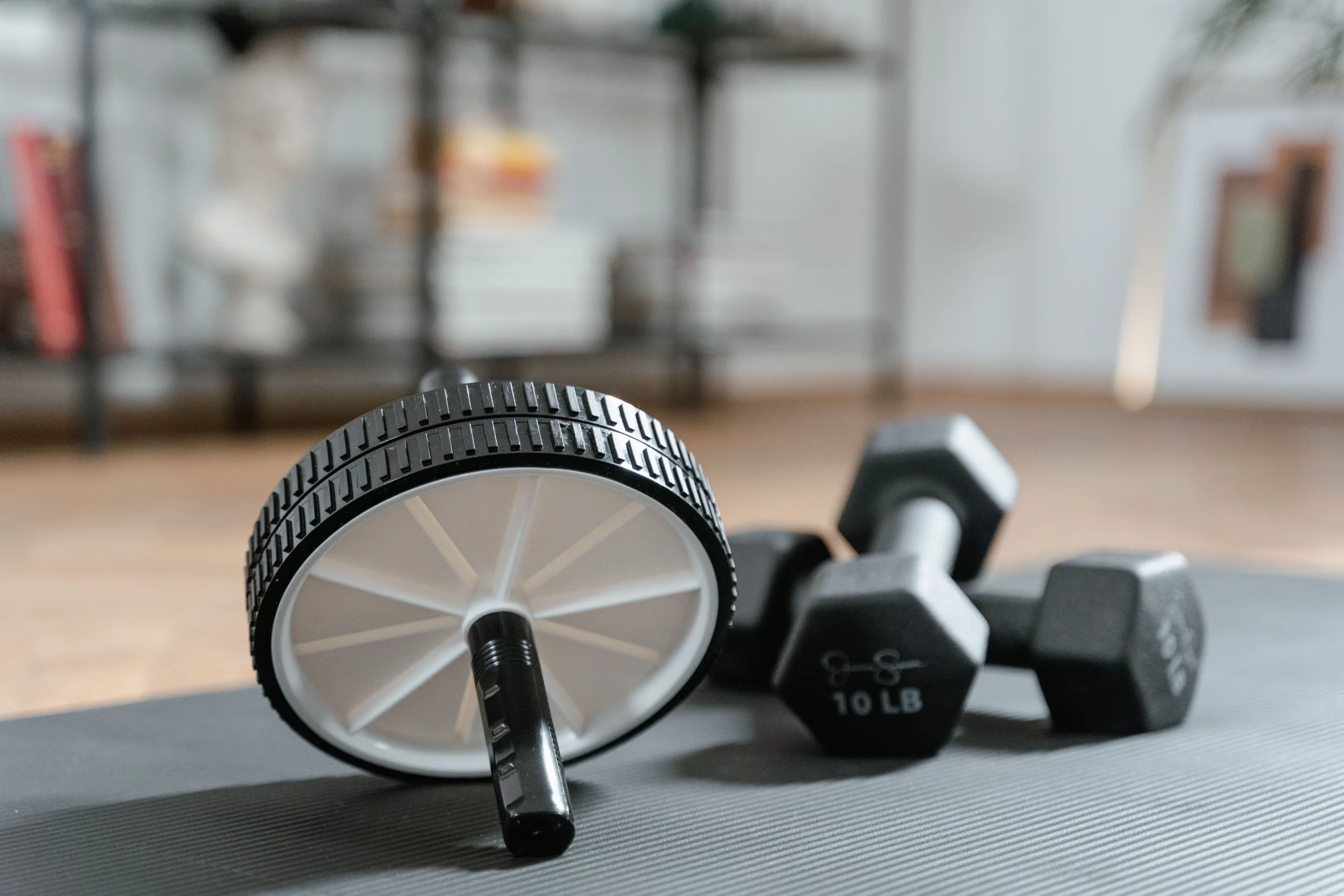 GD Ab Wheel Dumbbells scaled Ab wheel and dumbbells arranged on gym mat with gym equipment background