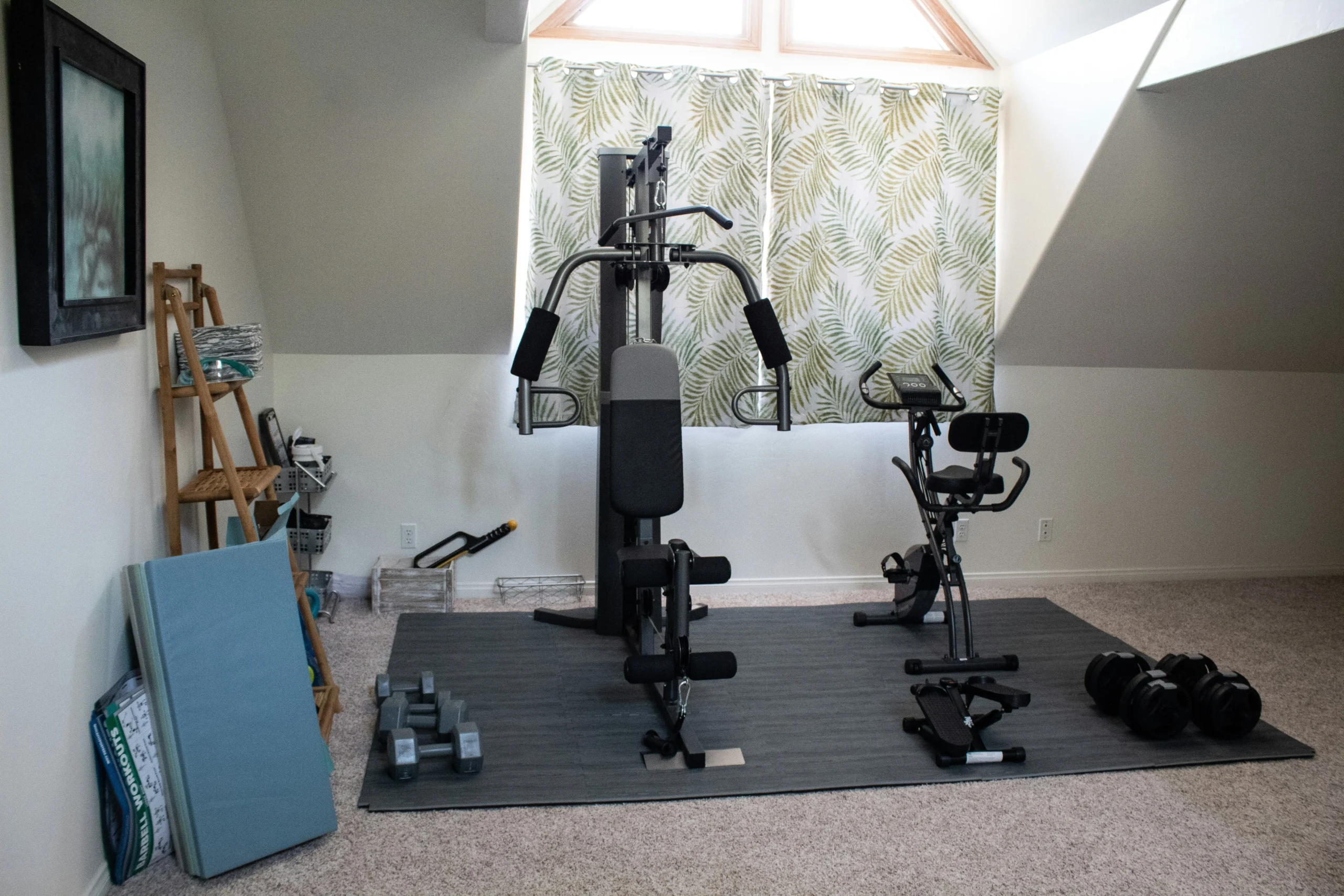 DIY gym home setup with gym home machine, exercise bike, and dumbbells in attic room