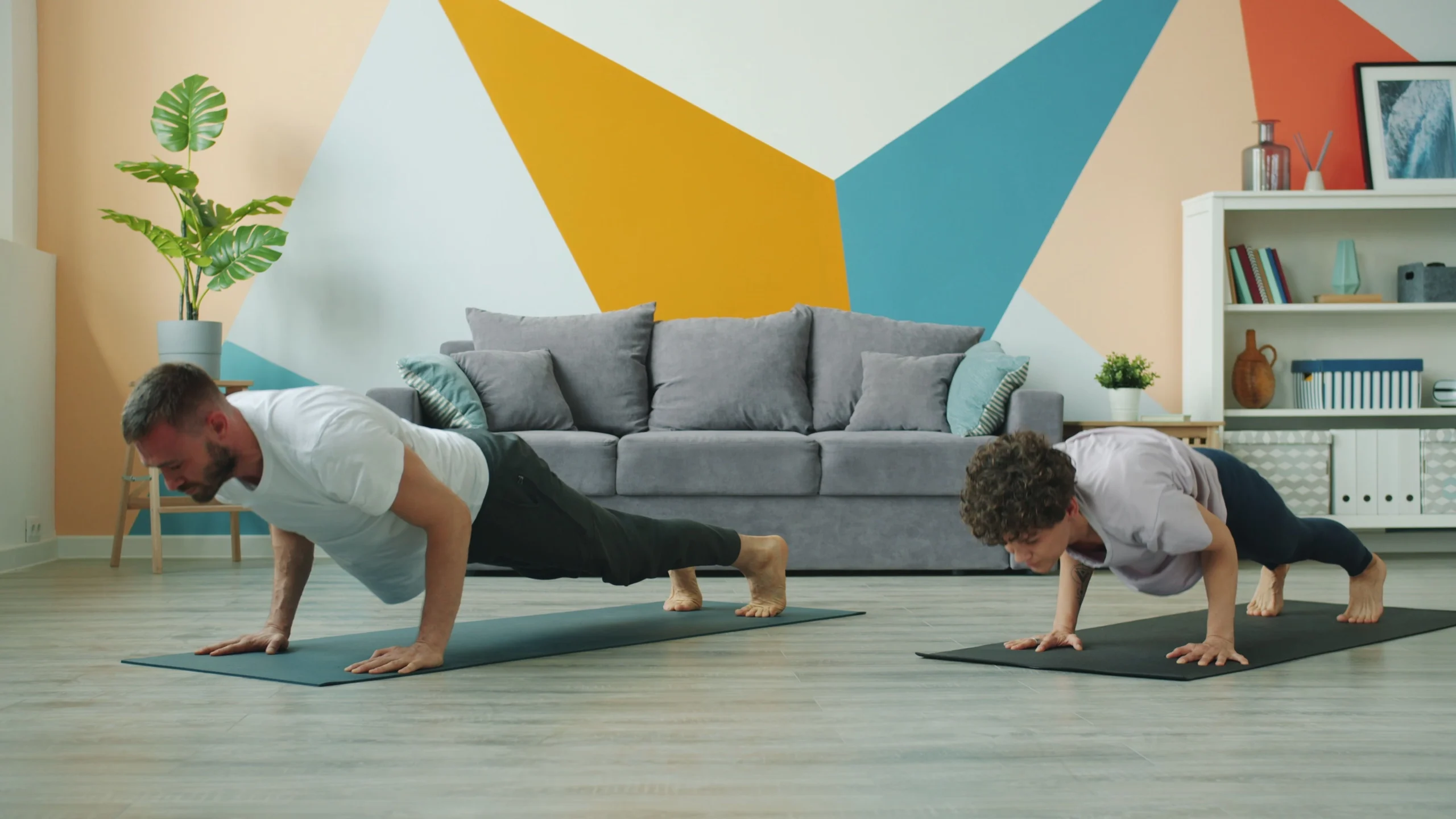 GD Workspace and Workout scaled Two people doing planks in modern living room with couch and colorful wall design