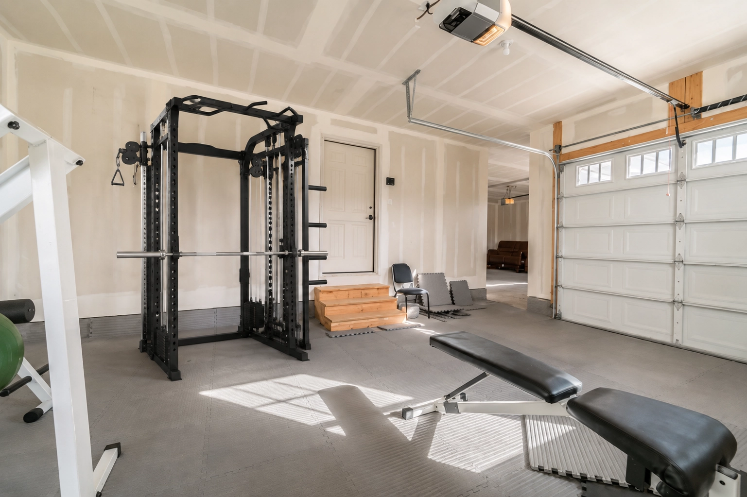 Black power rack with integrated pulley system in a garage gym home setup, featuring weight benches and training flooring
