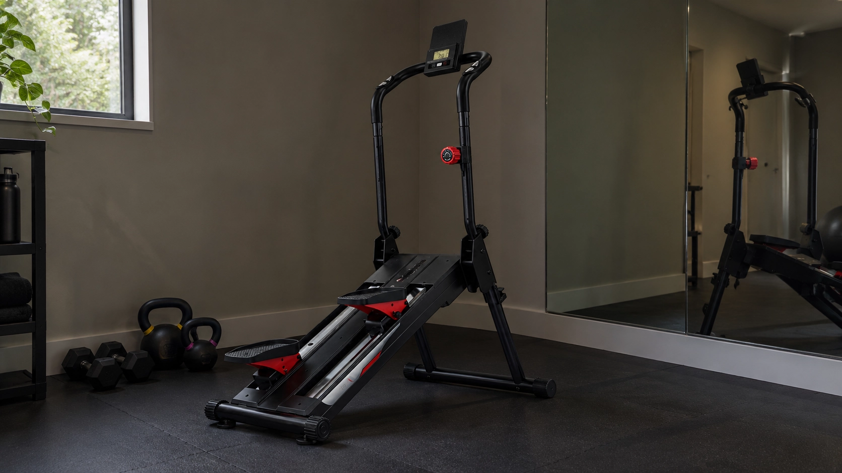 Black and red stair climber with digital display in a modern home gym space surrounded by kettlebells and floor-to-ceiling mirror, demonstrating cardio equipment setup