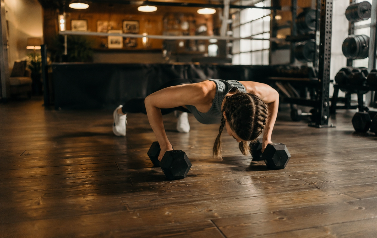 Woman performing a dumbbell floor press exercise with hexagonal weights in a fully equipped gym