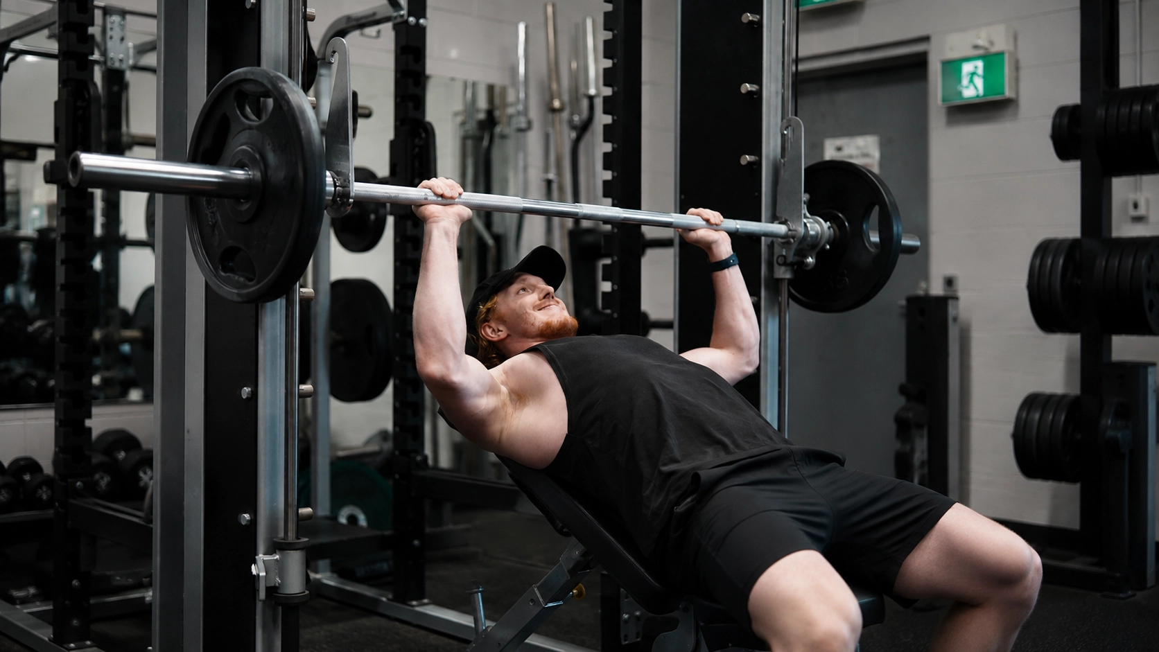 Man performing a bench press on a Smith machine with loaded barbell in a commercial gym