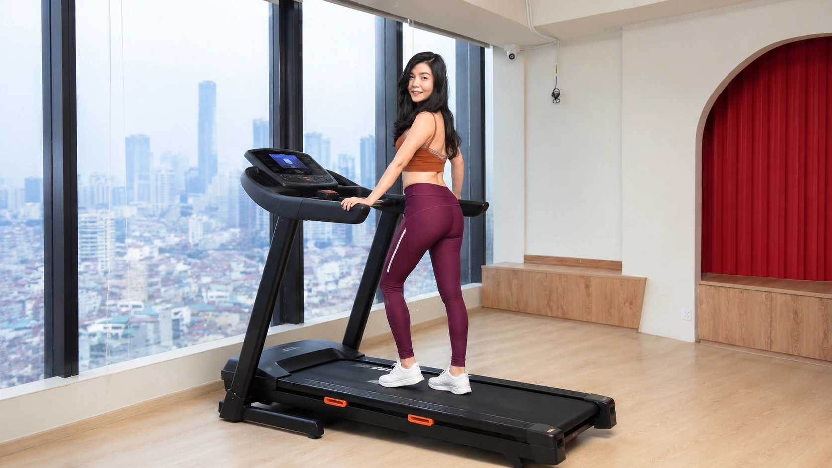 Woman standing on heavy-duty treadmill in modern high-rise apartment with city skyline view