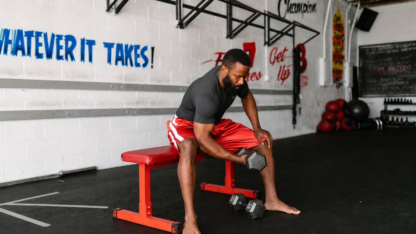 WB Leg Extension and Curl from 200 to 400 Man performing a dumbbell curl on a red weight bench with leg extension attachment in a home gym