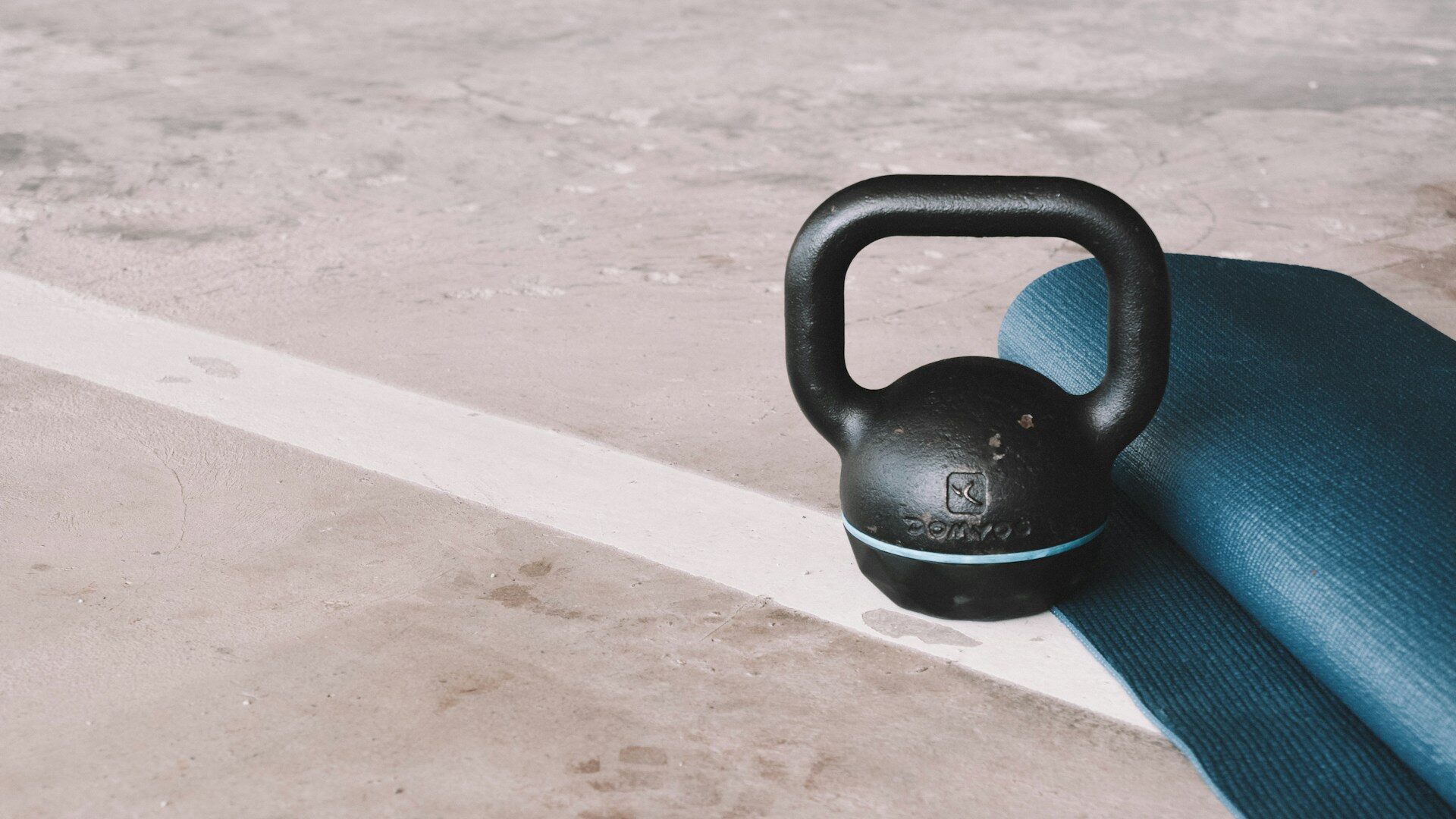 Black cast iron kettlebell resting on a light floor next to a mat