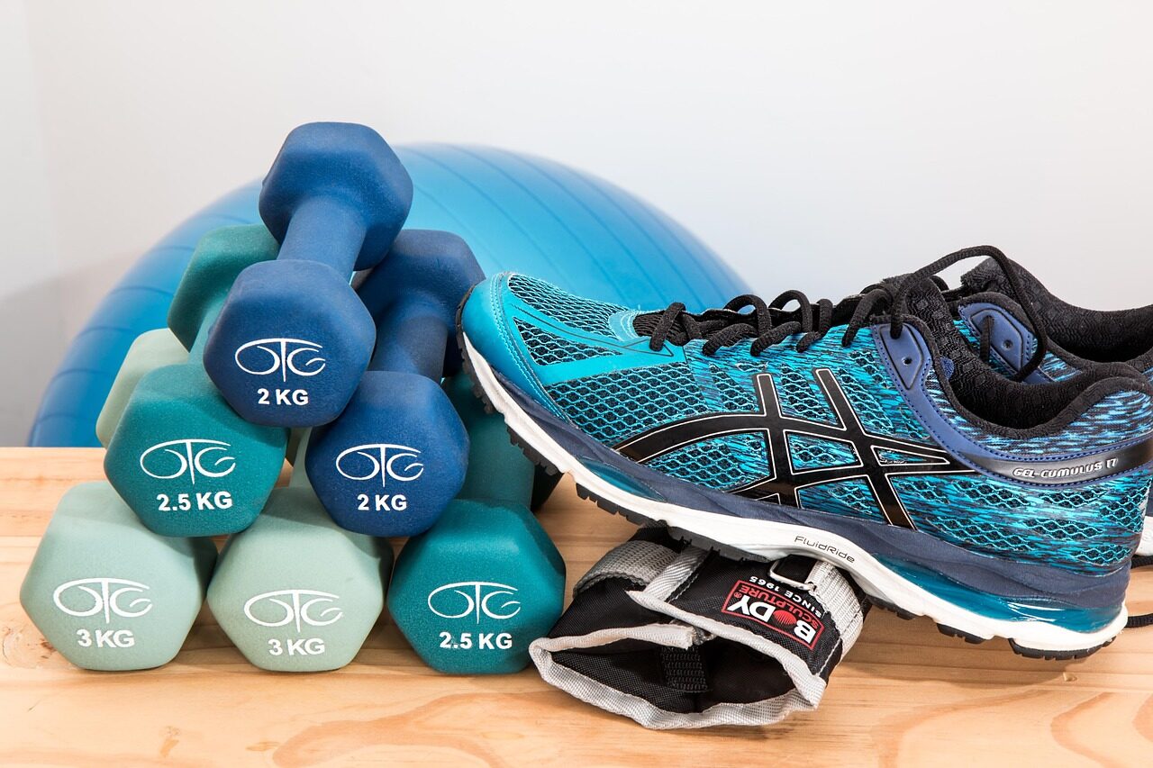 Light dumbbells, ankle weights and sneakers laid out next to an exercise ball