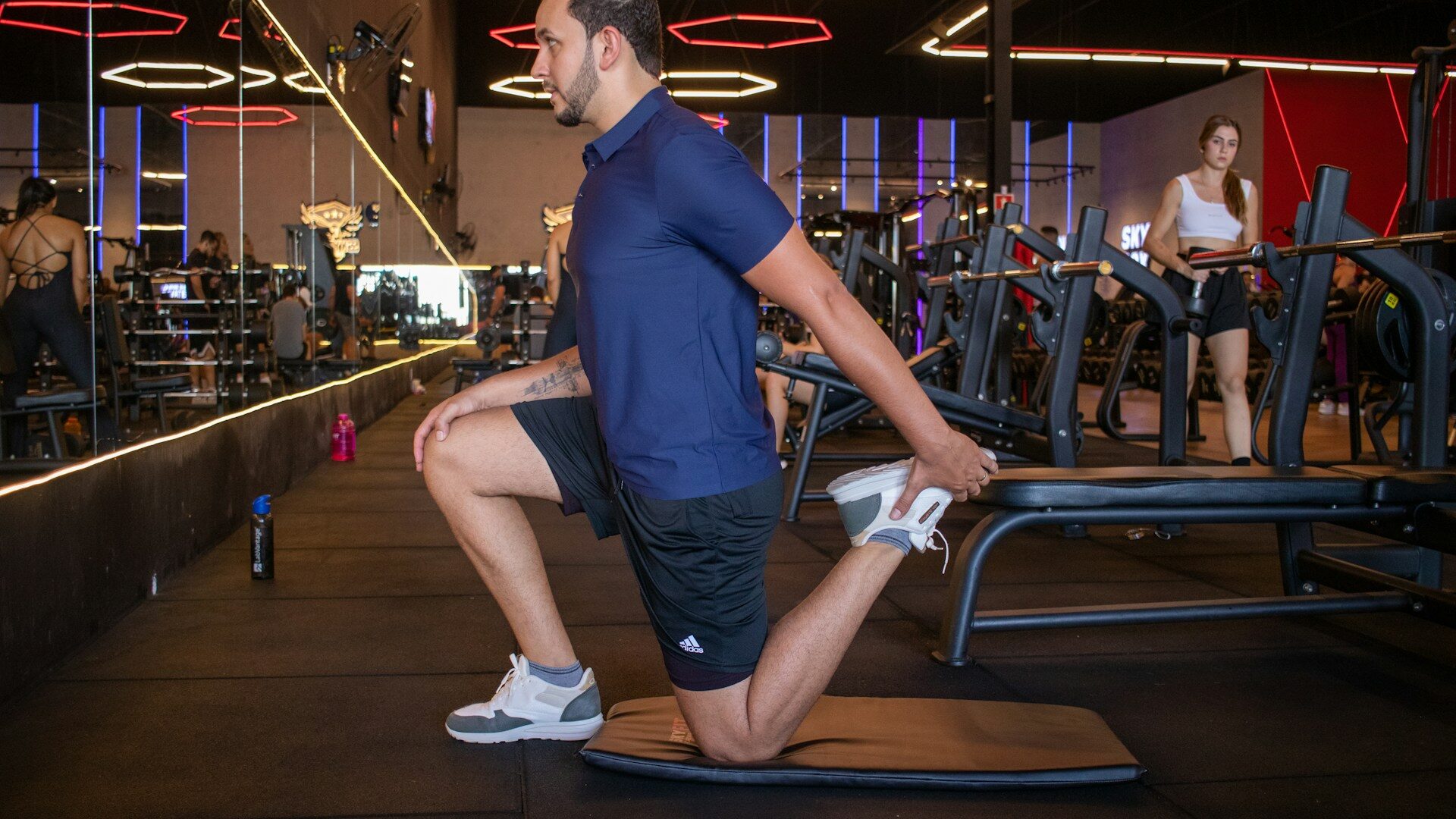 Man doing a half-kneeling hip flexor stretch on the gym floor after training