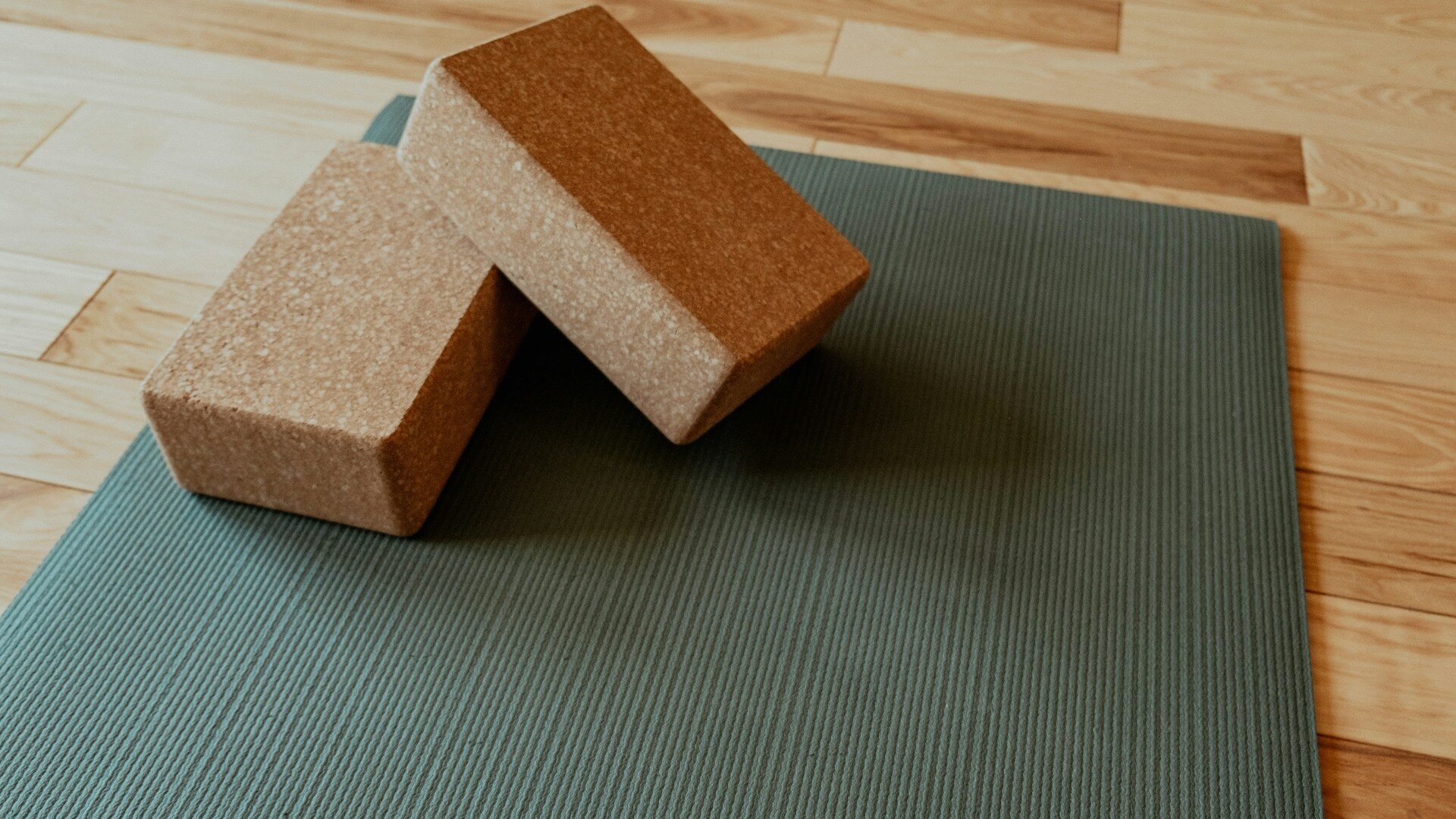 Two cork yoga blocks on a green yoga mat on a wooden floor