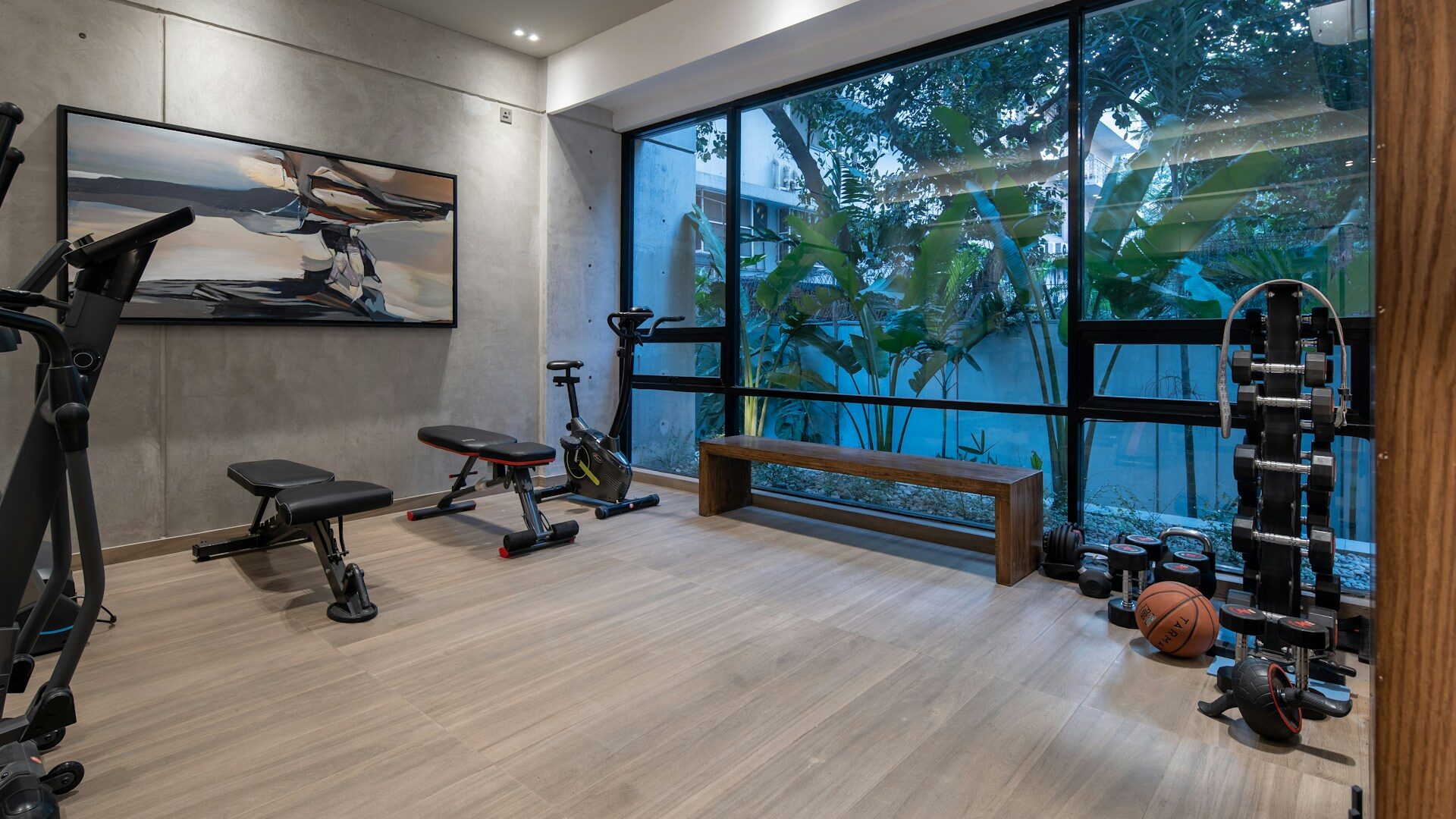 Well-equipped home gym with a bench, weight rack and cardio machine by large windows