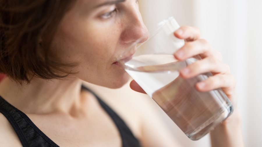 Woman drinking water bottle after elliptical workout to aid recovery and rehydration